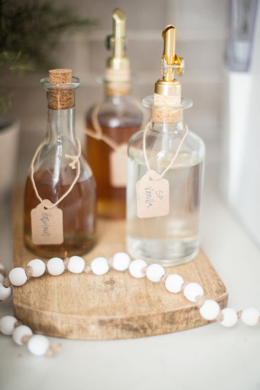 Handmade essential oil bottles with labels on a wooden tray for aromatherapy. Diffuser bottles with cork stoppers and gold spray top for homemade scents, surrounded by decorative beads.