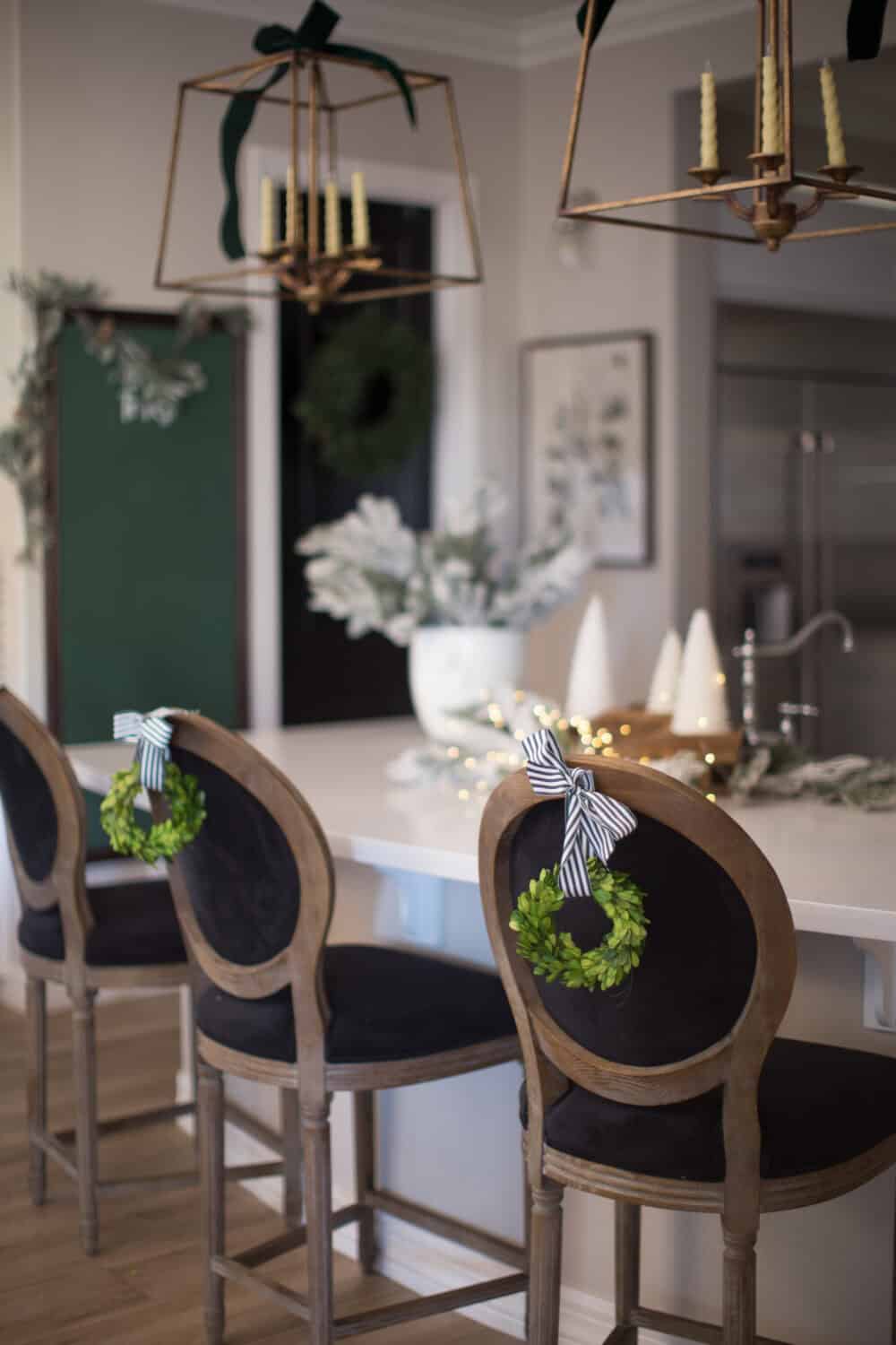 Festive holiday decor with green wreaths and black ribbon accents hanging on stylish wooden chairs in a modern kitchen, perfect for Christmas or winter celebrations.