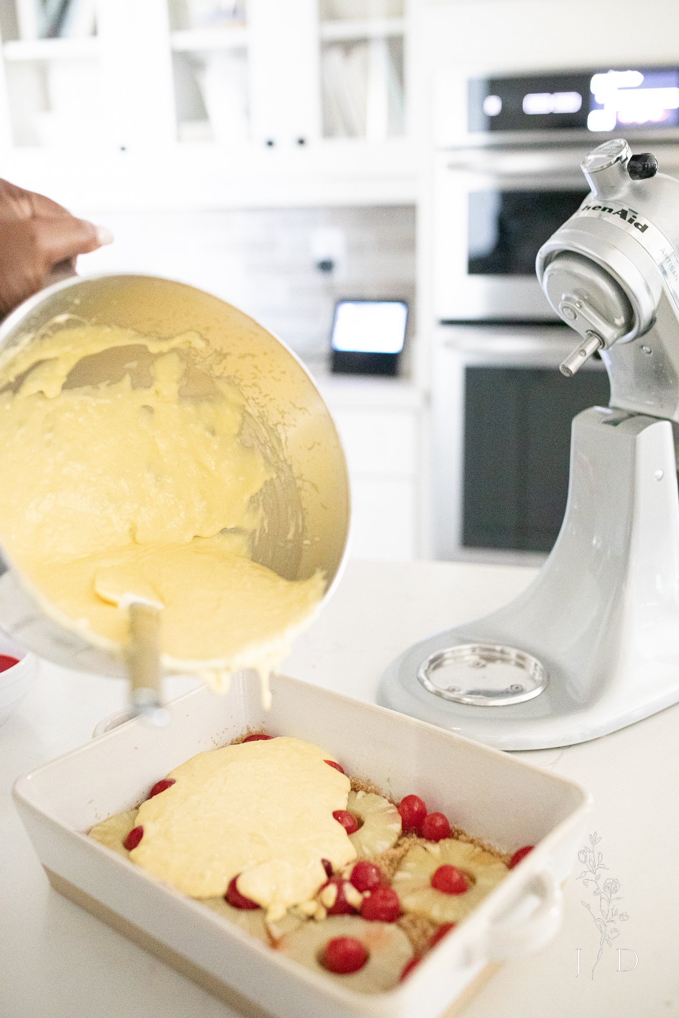 Cake batter pouring over pineapple, cherries and brown sugar. 